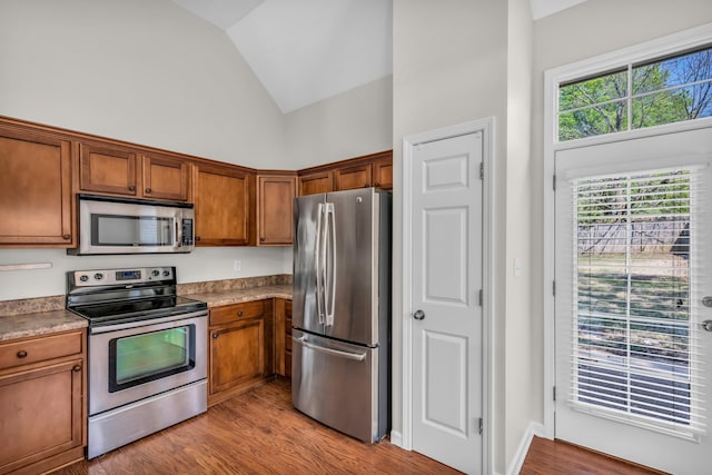 kitchen with lofted ceiling, stainless steel appliances, wood finished floors, and brown cabinets