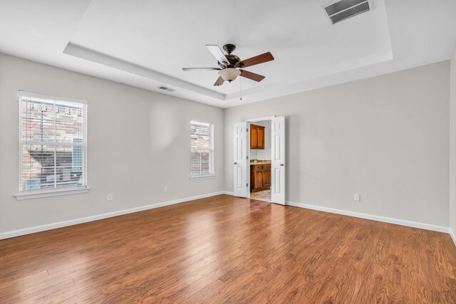empty room featuring a raised ceiling, dark wood-style flooring, a ceiling fan, and visible vents