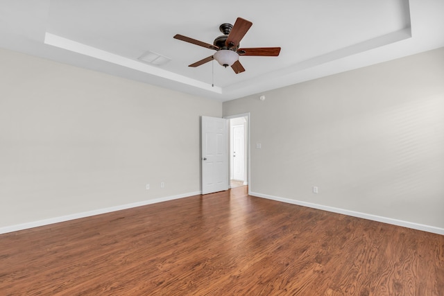 spare room featuring a tray ceiling, wood finished floors, baseboards, and a ceiling fan
