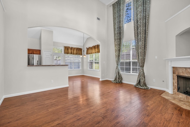 unfurnished living room with visible vents, baseboards, wood finished floors, a high ceiling, and a high end fireplace