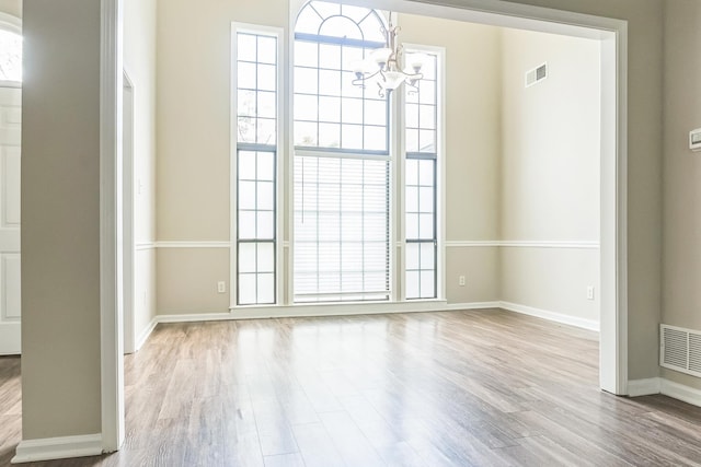 unfurnished dining area with a chandelier, wood finished floors, baseboards, and visible vents
