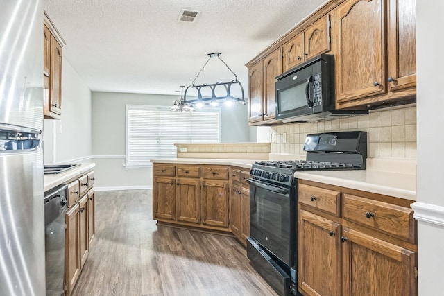kitchen featuring dark wood finished floors, a peninsula, visible vents, black appliances, and light countertops