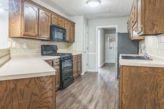 kitchen featuring dark wood-style flooring, light countertops, a textured ceiling, black appliances, and backsplash