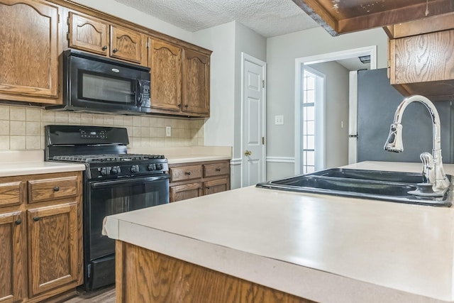 kitchen with light countertops, a sink, black appliances, and decorative backsplash