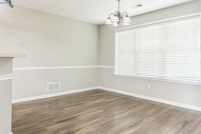spare room with wood finished floors, a notable chandelier, and visible vents
