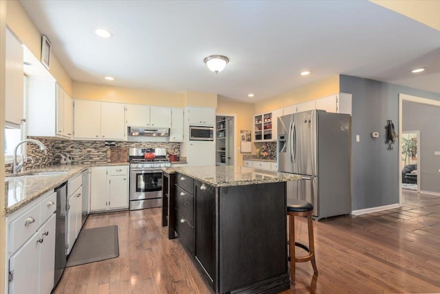 kitchen featuring backsplash, a kitchen island, stainless steel appliances, a sink, and wood finished floors
