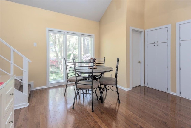 dining room featuring wood finished floors, high vaulted ceiling, baseboards, and stairs