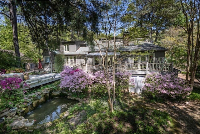 back of house featuring a small pond, a wooden deck, and a chimney