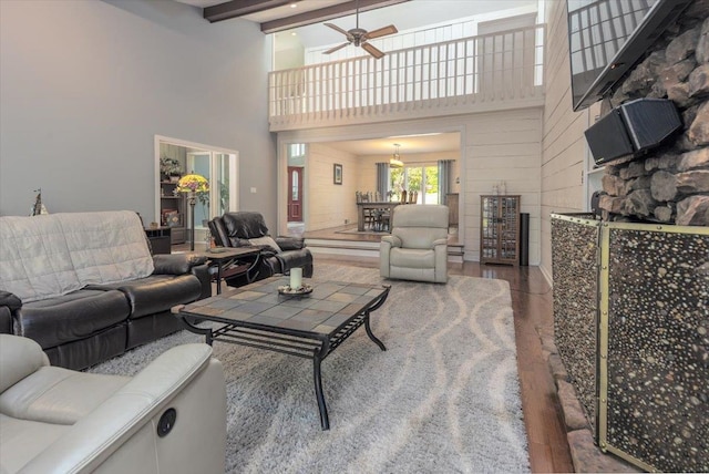 living area featuring a towering ceiling, ceiling fan, beamed ceiling, and wood finished floors