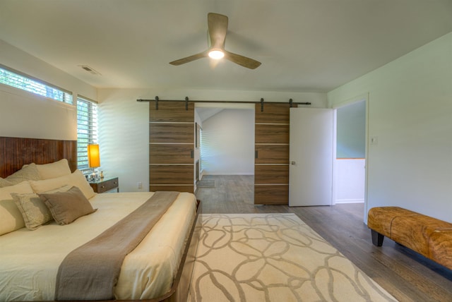 bedroom featuring visible vents, a ceiling fan, wood finished floors, and a barn door