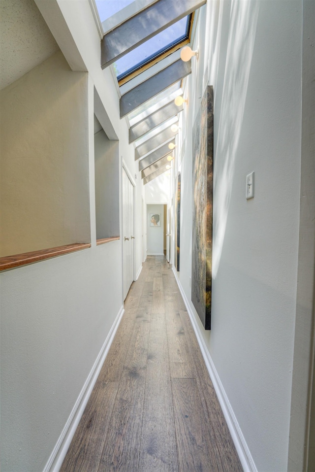 corridor with a skylight, baseboards, and wood finished floors