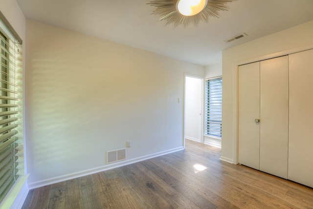 unfurnished bedroom with baseboards, wood finished floors, visible vents, and a closet
