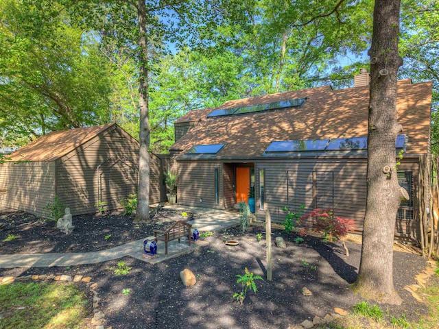 rear view of property with a chimney, roof with shingles, an outbuilding, and solar panels