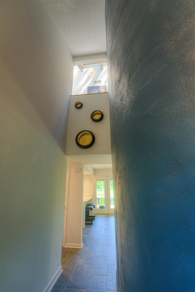 corridor featuring baseboards, a high ceiling, and a textured ceiling