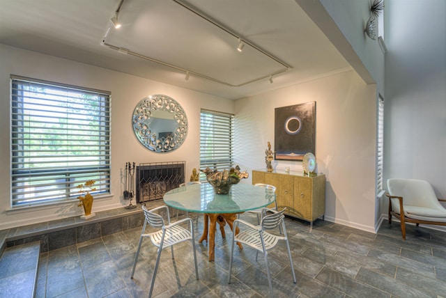 dining room with track lighting, a wealth of natural light, a fireplace with raised hearth, and baseboards