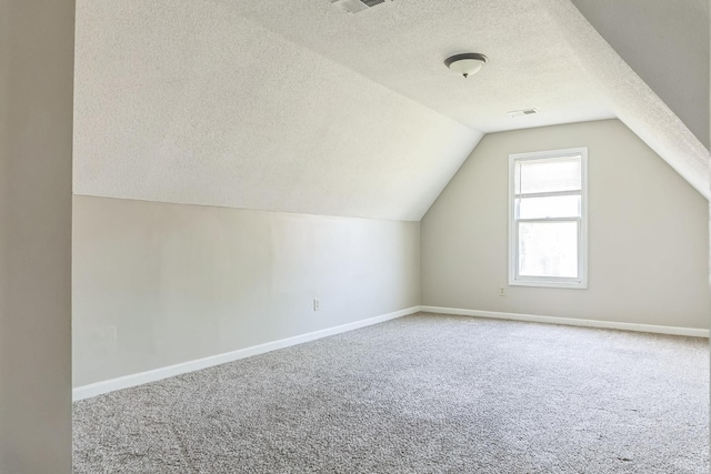 additional living space featuring baseboards, vaulted ceiling, carpet flooring, and a textured ceiling