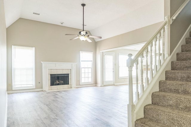 unfurnished living room with plenty of natural light, wood finished floors, stairway, ceiling fan, and a tile fireplace