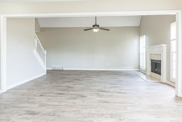 unfurnished living room featuring high vaulted ceiling, stairs, light wood-style floors, ceiling fan, and a tiled fireplace