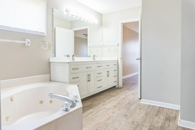 bathroom with double vanity, a jetted tub, wood finished floors, a sink, and baseboards