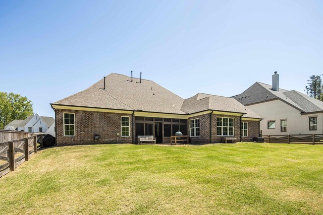 rear view of house featuring a shingled roof, a fenced backyard, a yard, brick siding, and a sunroom