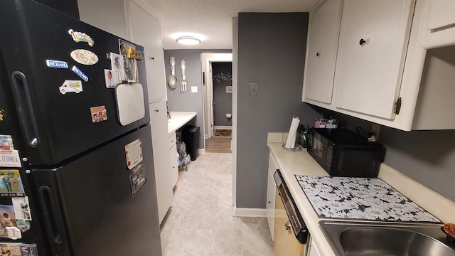 kitchen with a sink, black appliances, light countertops, baseboards, and white cabinetry