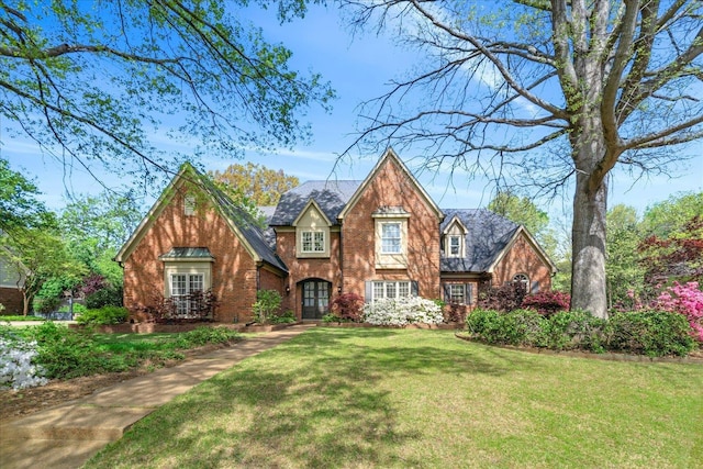 tudor house with french doors, a front lawn, and brick siding