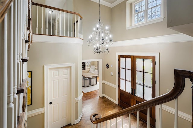 foyer entrance featuring a towering ceiling, ornamental molding, french doors, baseboards, and a notable chandelier