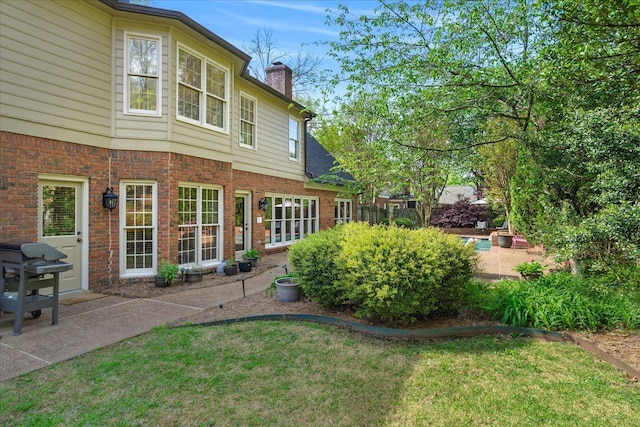 back of house with a lawn, a chimney, brick siding, and a patio area