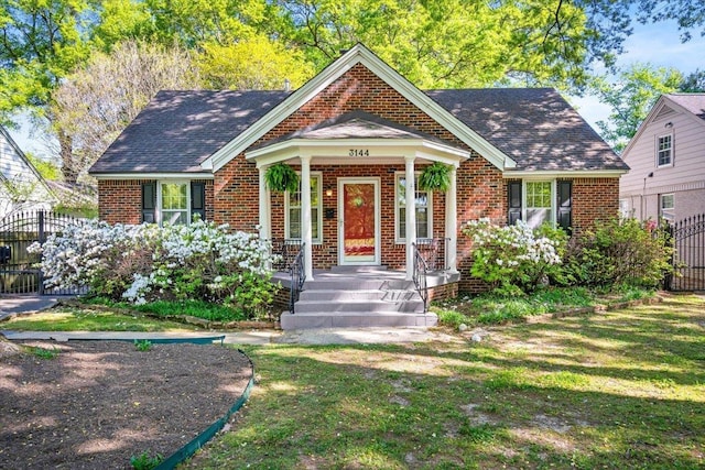 bungalow-style home with brick siding, a front lawn, fence, and a porch