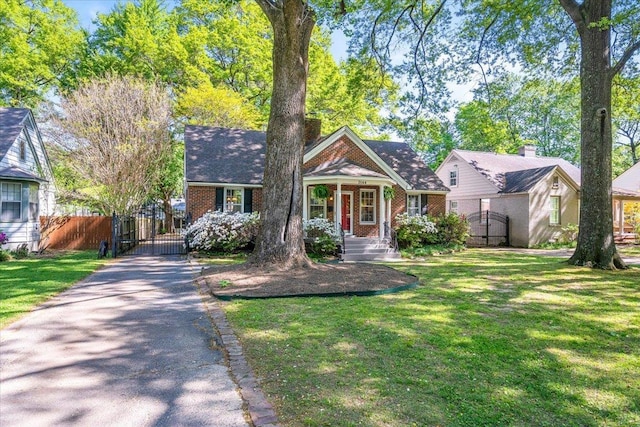 view of front of house featuring a front lawn, a gate, driveway, fence, and brick siding