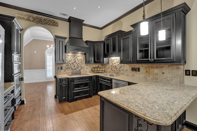 kitchen with a sink, dark cabinetry, custom range hood, appliances with stainless steel finishes, and visible vents