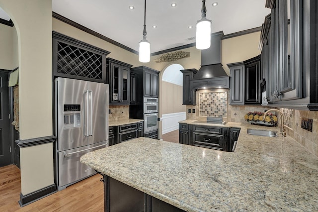 kitchen with stainless steel appliances, a sink, dark cabinetry, crown molding, and premium range hood