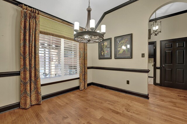 unfurnished dining area featuring baseboards, wood finished floors, a chandelier, and crown molding