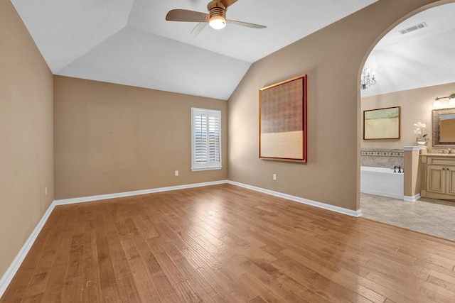 interior space with arched walkways, light wood finished floors, ensuite bath, lofted ceiling, and visible vents