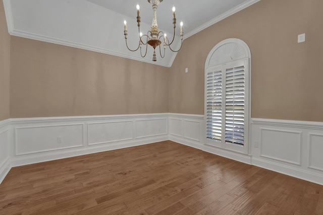unfurnished dining area featuring wainscoting, wood finished floors, a notable chandelier, and crown molding