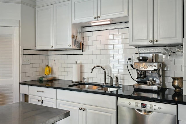 kitchen featuring white cabinets, dark countertops, stainless steel dishwasher, and a sink