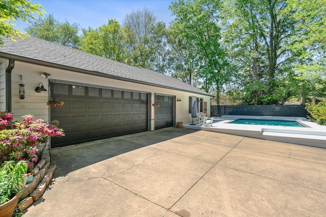 garage with driveway, fence, and a fenced in pool