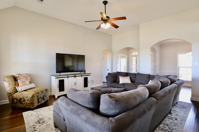 living area featuring baseboards, arched walkways, dark wood-type flooring, and ceiling fan