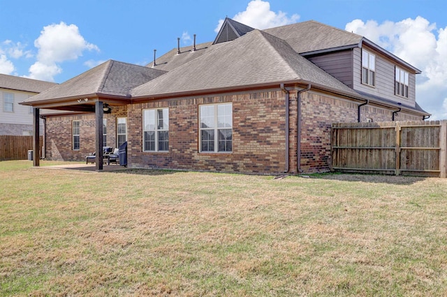 rear view of property featuring a patio area, a shingled roof, fence, a yard, and brick siding