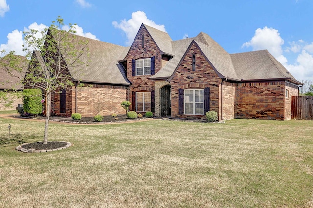 view of front of house featuring brick siding, fence, roof with shingles, and a front yard