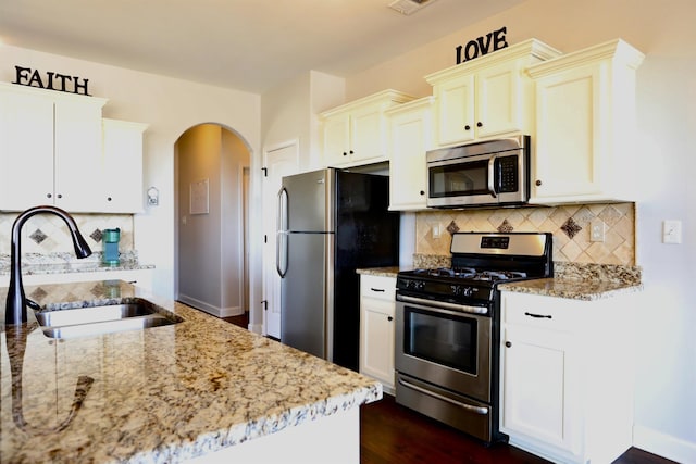 kitchen featuring light stone counters, a sink, decorative backsplash, arched walkways, and stainless steel appliances