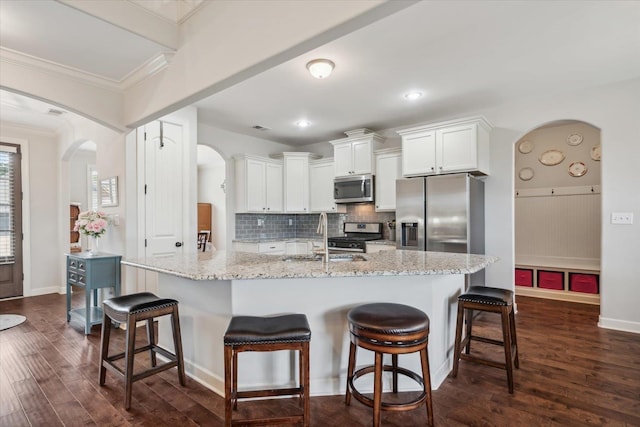 kitchen with crown molding, a sink, arched walkways, stainless steel appliances, and dark wood finished floors