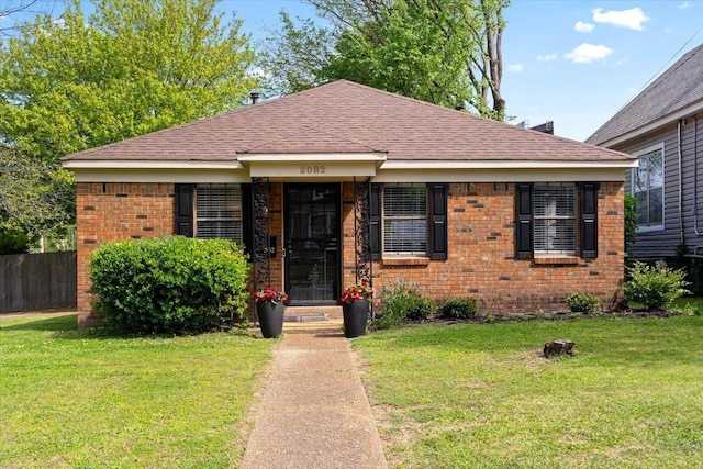 bungalow-style home featuring brick siding, fence, a shingled roof, and a front yard