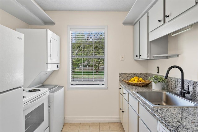 kitchen with a sink, stacked washing maching and dryer, light tile patterned flooring, white appliances, and baseboards