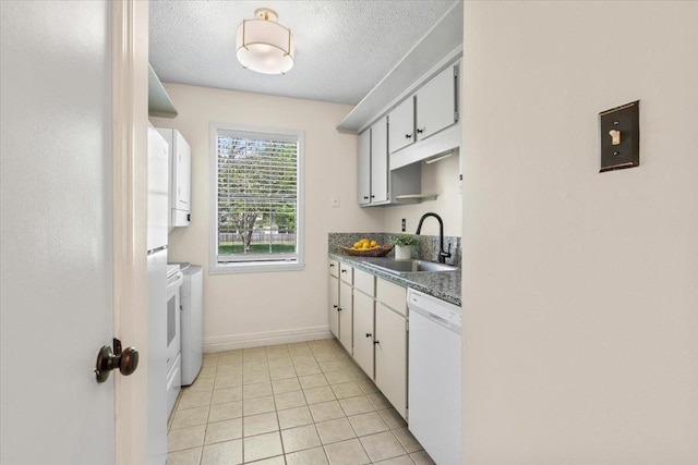kitchen featuring independent washer and dryer, a sink, dark countertops, white dishwasher, and baseboards