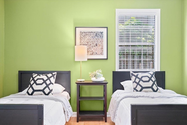 bedroom with multiple windows, wood finished floors, and baseboards