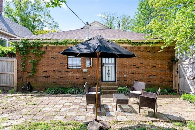 rear view of house featuring brick siding, fence, a shingled roof, entry steps, and a patio area