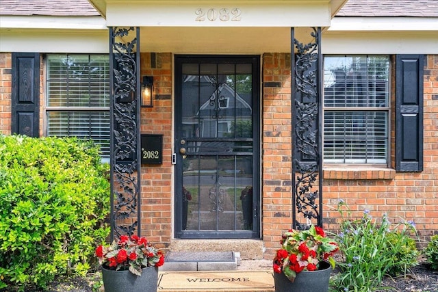 entrance to property featuring a shingled roof, covered porch, and brick siding
