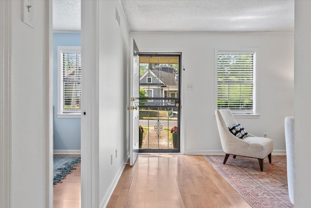 doorway with crown molding, a textured ceiling, wood finished floors, and baseboards