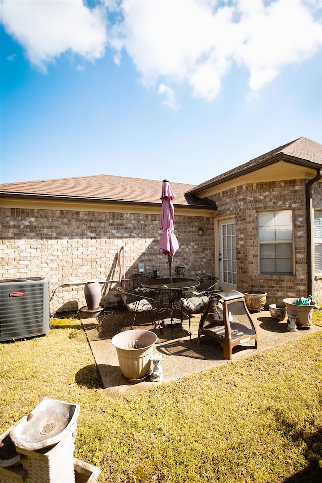 rear view of property with brick siding, cooling unit, a patio area, and a lawn